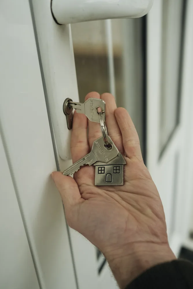 Hand holding house keys at a front door, ready for handover